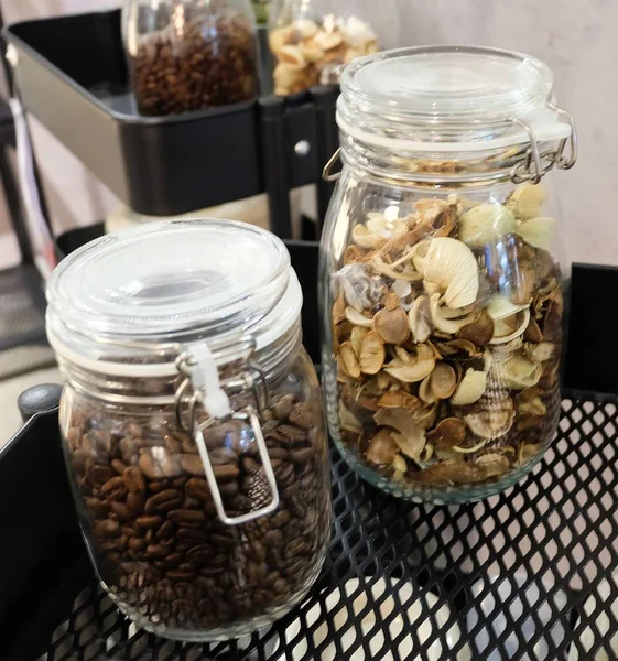 Mutfak malzemesi, kavrulmuş kahve çekirdekleri ve gümüş kapaklı cam kavanozlara kokulu çiçek.