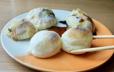 Bir çift çubuk taze ızgara Japon mochi pirinç keki tutar, üzerine tatlı soya sosu damlatır. Görüntü basit Asya atıştırmalıklarını ön plana çıkarıyor..