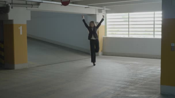 年轻有吸引力的女商人穿着正式西装跳跃和滑稽的舞蹈在地下停车场在她的途中到汽车 — 图库视频影像