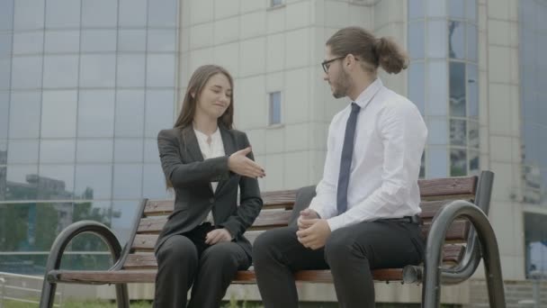 笑顔とビジネスの取り引きの閉鎖本社ビル手前のベンチで手を揺することによって条約を作る形式的なスーツを着た若いビジネス人 — ストック動画
