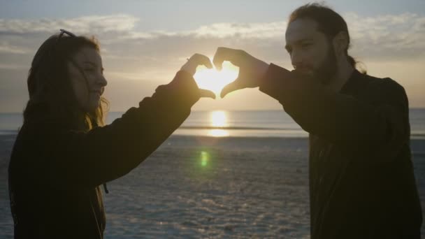 Genç çift gün batımından önce başlarını sahilde bir kalp şekil verme — Stok video