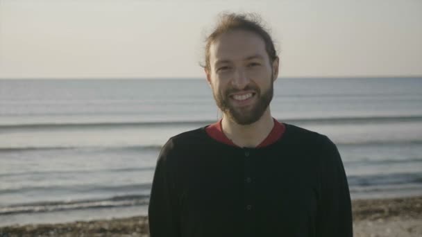 Крупный план портрета привлекательного мужчины, улыбающегося на пляже на восходе солнца — стоковое видео
