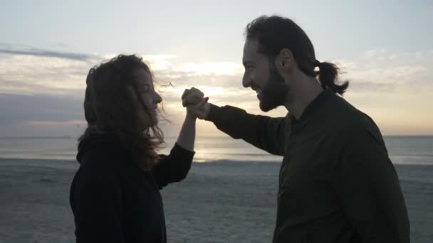 Gyönyörű pár élvezi a naplementét a kezét, és így a szív alakú lassítva csók strand — Stock videók