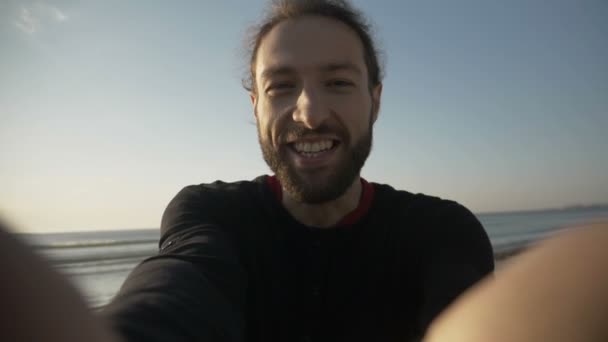 Молодий чоловік в соціальних мережах грає, розважаючись і маючи відеодзвінок на красивому заході сонця на пляжі в повільному русі — стокове відео