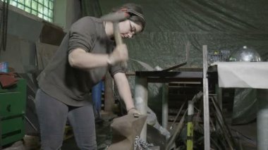 DIY onun atölyesinde düzleştirmek için karşı kulaklıklar giyen ve bir metal çubuğu çekiç kadın demirci