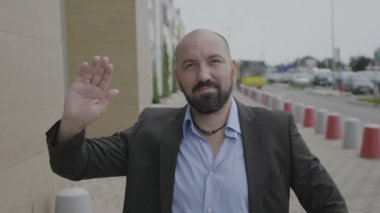 Selam pozitif kendine güvenen gülümseme ile genel şehir sokak üzerinde elini sallayarak takım elbiseli dostça adam