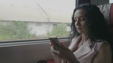 Genç yolcu kadın banliyö kulaklık kullanarak ve smartphone kablosuz internet tarafından bağlı sohbet müzik dinlerken tren ile seyahat