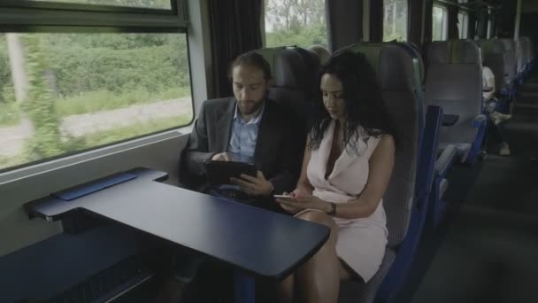 在平板电脑上工作的年轻企业家男性在商务旅行中与坐在火车上的女商人讨论 — 图库视频影像