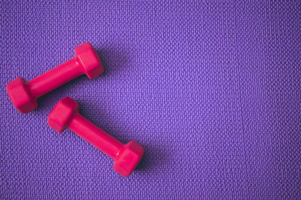 Top view of purple yoga mat with bright pink dumbbells with copy space