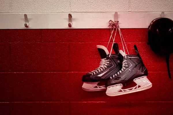 Hockey skates and helmet hanging in locker room with red gradient background and copy space