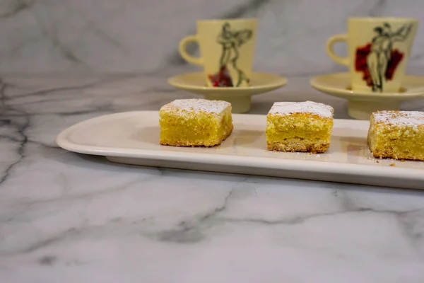 Tray with home baked lemon squares, lemon bars, with two tango painted cups over white marbled background