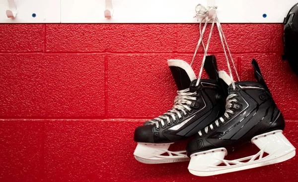 Hockey skates and helmet hanging in locker room with copy space in red background