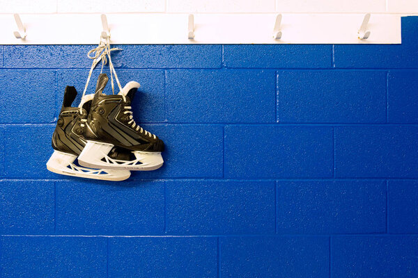 Hockey skates hanging over blue wall in locker room with copy space 