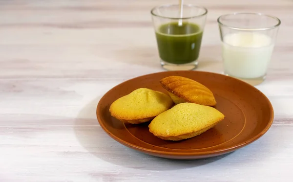 Madeleines, matcha tea and milk in wooden rustic background with copy space