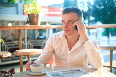 Kafede kahve içme ve telefon kullanarak bir genç adam. İş açık havada portre.