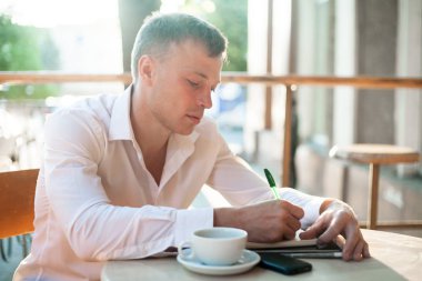 Not Defteri veya smartphone ve kahve açık kafede masada planlayıcısı yazma adam.