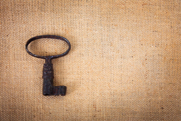 An ancient metal key on the background of sacking. Background in vintage style.