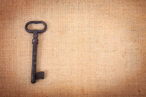 An ancient metal key on the background of sacking. Background in vintage style.