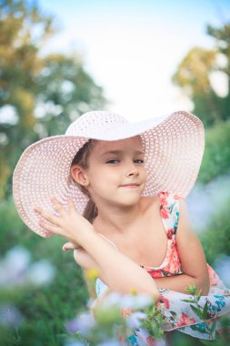 Çiçekler arasında yeşil bir bahçe içinde yaz aylarında pembe şapkalı güzel kız.