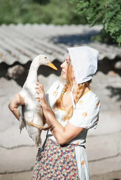 A woman in a village dressed in country style is holding a goose. Shooting in retro style.