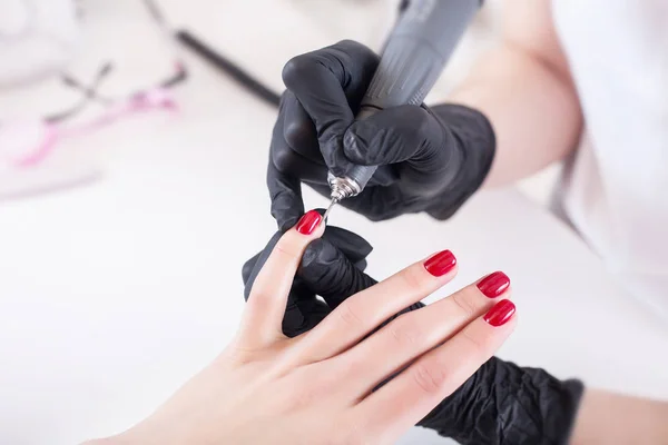 Manicurist, nail artist handles nails with manicure milling cutter. Beauty service, nail salon, health care and cosmetics. Close up.