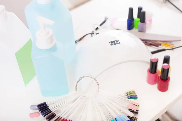 Manicure set for gel nail procedure - Nail LED lamp, colour gel polishes, disinfectants and other accessories on white table.