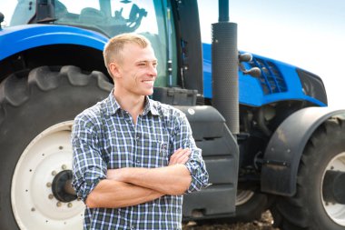 Genç çekici adamın yanına bir traktör. Tarım ve alan çalışmaları kavramı.