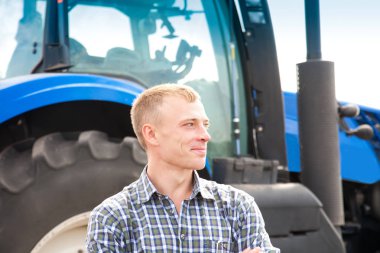 Genç çekici adamın yanına bir traktör. Tarım ve alan çalışmaları kavramı.