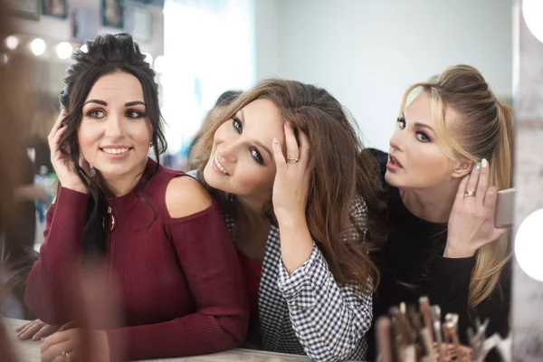 Drie jonge vrouwen kijken in de spiegel in de schoonheidssalon. — Stockfoto