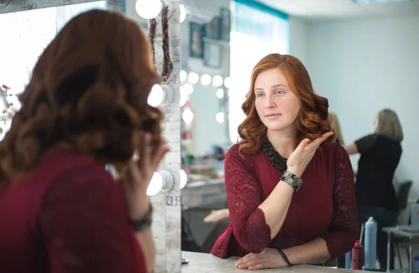Femme dans un salon de beauté regarde son reflet dans le miroir et vérifie la coiffure . — Photo