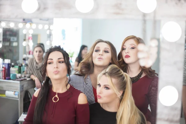 Cuatro mujeres jóvenes mirándose en el espejo en el salón de belleza . — Foto de Stock