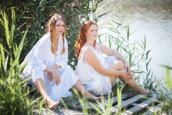 Deux jeunes femmes en longues robes blanches près de la rivière . — Photo