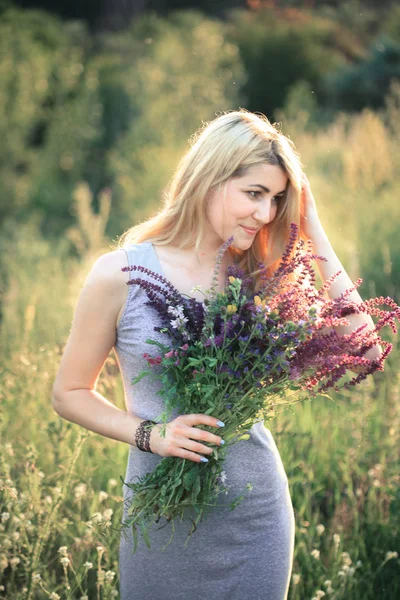 Retrato de una joven mujer hermosa en la naturaleza con un ramo de flores . — Foto de Stock