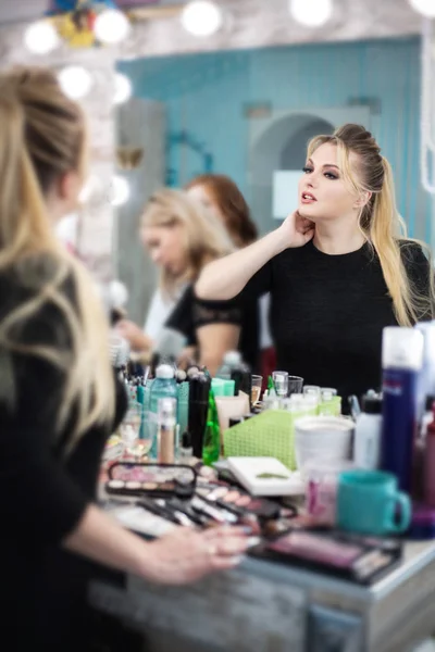 Mujer en un salón de belleza mira su reflejo en el espejo en su maquillaje y peinado . — Foto de Stock