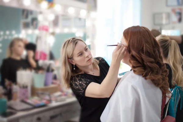 Artista de maquillaje profesional que trabaja en la mujer joven hace maquillaje en el salón de belleza —  Fotos de Stock