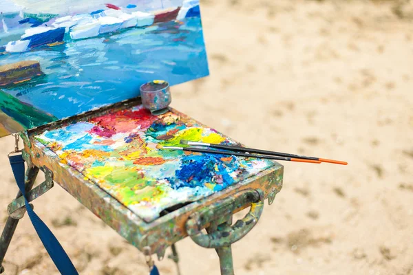 Colorful workplace of the artist with brushes and oil paints in the open air — Stock Photo, Image