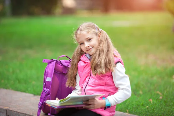 Schoolmeisje met een rugzak en boek buiten. Onderwijs-en Leerconcept. — Stockfoto