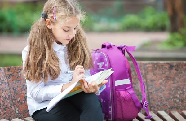 Schoolgirl with a backpack and book outdoors. Education and learning concept. — Stock Photo, Image