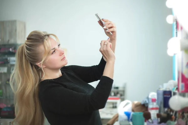 Молодая женщина с профессиональным макияжем делает селфи у зеркала . — стоковое фото