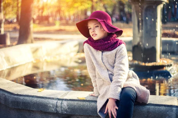 Fille en manteau classique et chapeau dans le parc d'automne près de la fontaine. Saison d'automne, mode, enfance . — Photo