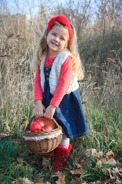 Niña en ropa acogedora con manzanas en el fondo dorado de otoño . —  Fotos de Stock