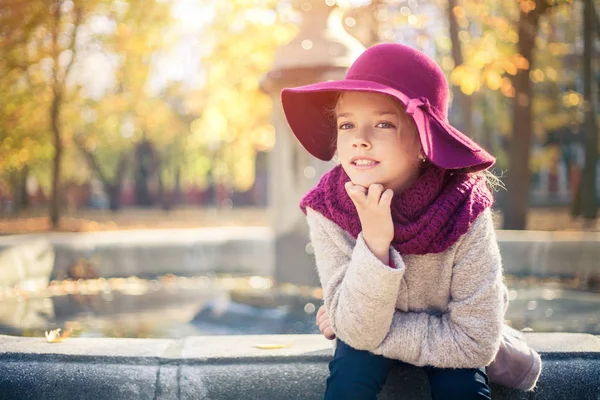 Ragazza in cappotto classico e cappello nel parco autunnale vicino alla fontana. Stagione autunnale, moda, infanzia . — Foto Stock