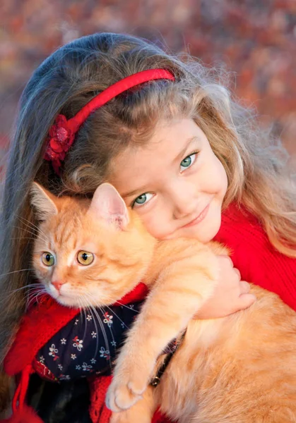 Porträt eines kleinen Mädchens mit einer roten Katze in den Händen im Herbst. — Stockfoto