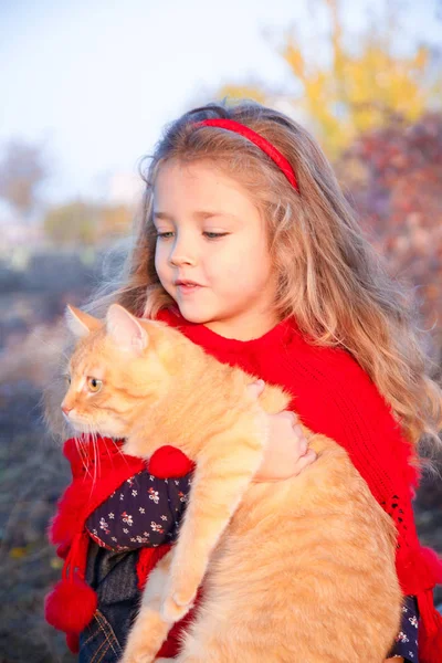 Porträt eines kleinen Mädchens mit einer roten Katze in den Händen im Herbst. — Stockfoto