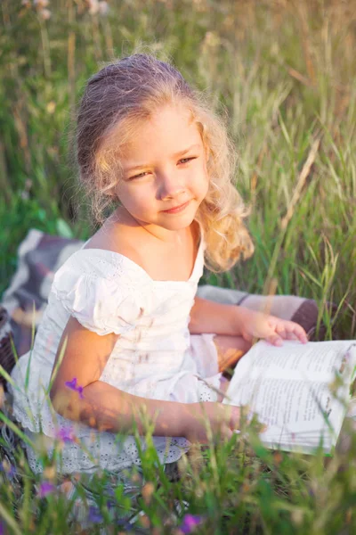 Little girl with a book in her hands on a meadow in a summer day. — Stock Photo, Image
