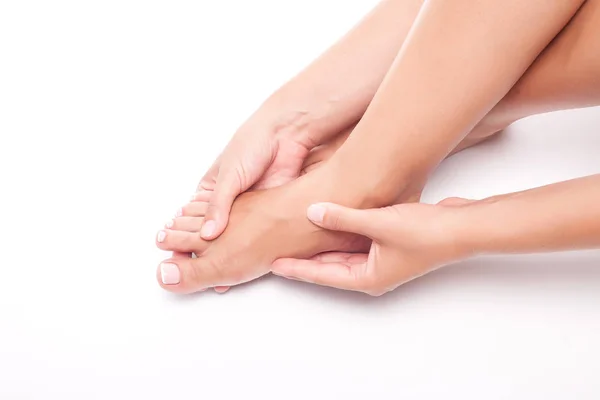 Mulher massageia um pé dolorido no fundo branco no estúdio . — Fotografia de Stock