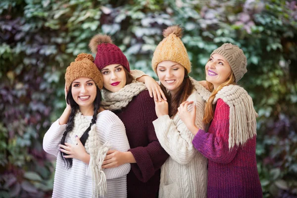 Quatro mulheres melhores amigos abraçando no parque em um cachecol de malha e chapéus . — Fotografia de Stock