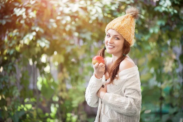 Feliz estilo de vida retrato de una hermosa joven en un cálido sombrero de otoño con una manzana en la mano . —  Fotos de Stock