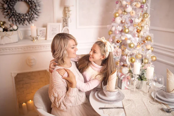 Hermosa madre joven con su hija en el interior de Año Nuevo en la mesa cerca del árbol de Navidad . — Foto de Stock