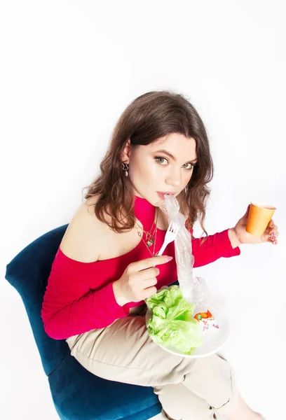 Young beautiful woman eating a plastic bag as a concept of plastic contaminated food. Ecology and healthy eating concept. Studio shot.. Hight quality photo